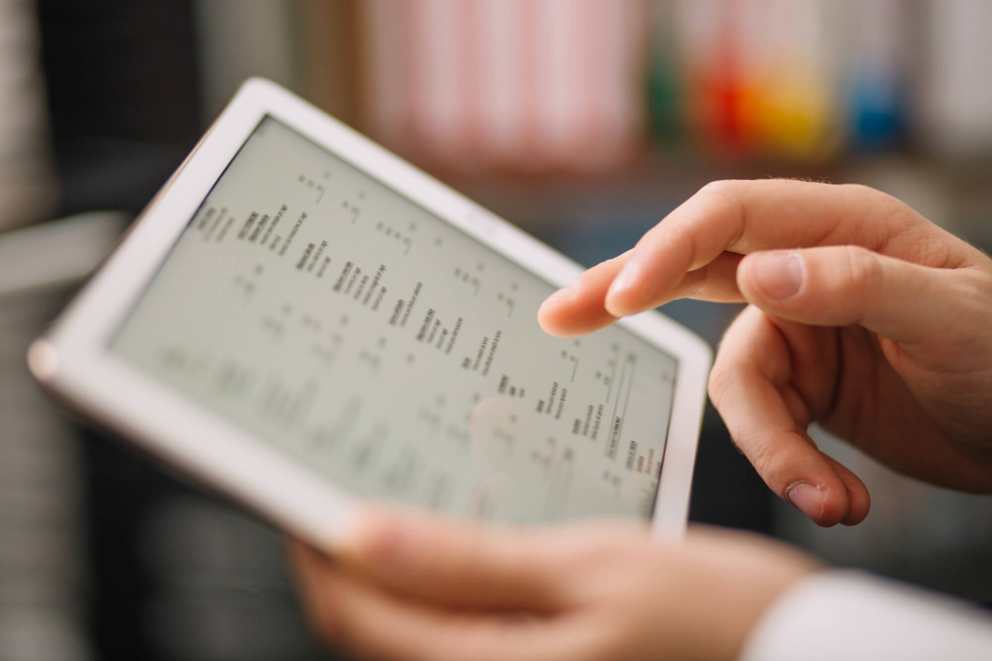 Primo piano di una persona che utilizza un tablet su cui sono visualizzati grafici e analisi dei dati, in un ambiente di lavoro moderno.