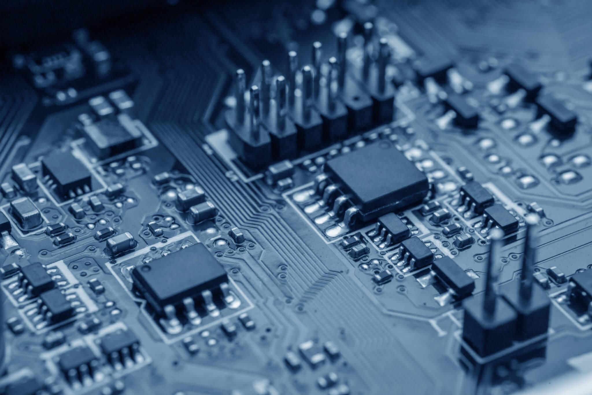 Nahaufnahme von Mikrochips und elektronischen Bauteilen, die auf einer blauen Leiterplatte montiert sind, mit sichtbaren Anschlüssen und Pins.
