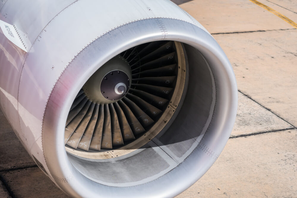Un gros plan détaillé du turboréacteur d'un avion commercial, montrant les pales numérotées de la soufflante et le capot d'admission sur une piste en béton.